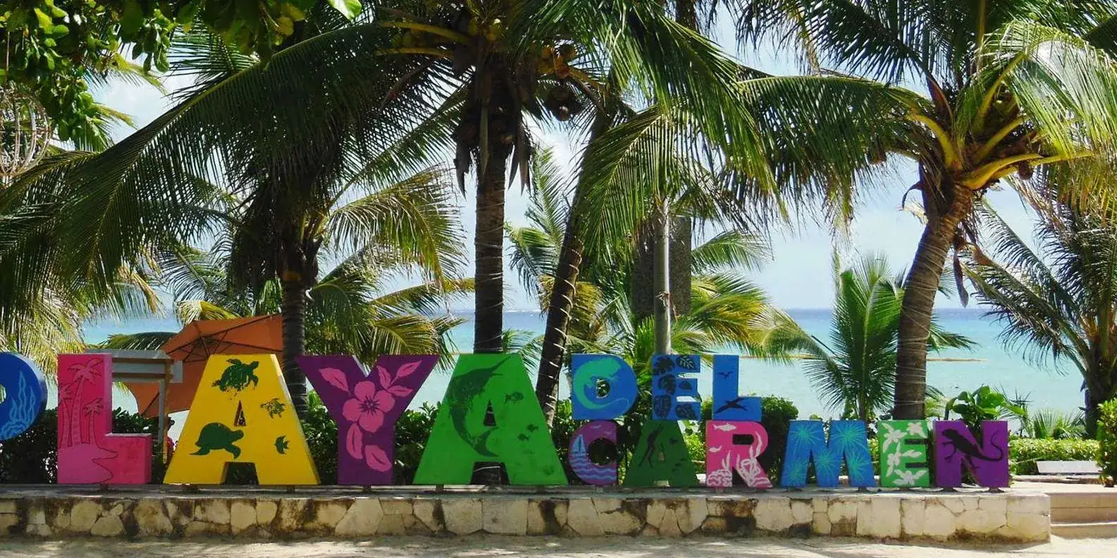Playa del Carmen sign beneath palm trees